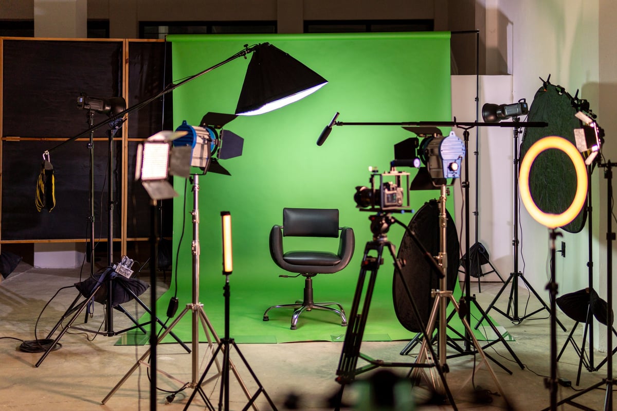 Green screen studio set up with camera, lights, and chair for video production