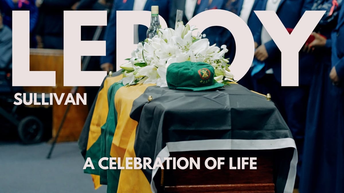 Casket draped with green and gold cloth, topped with white flowers, with Leroy Sullivan branding and A Celebration of Life text overlay